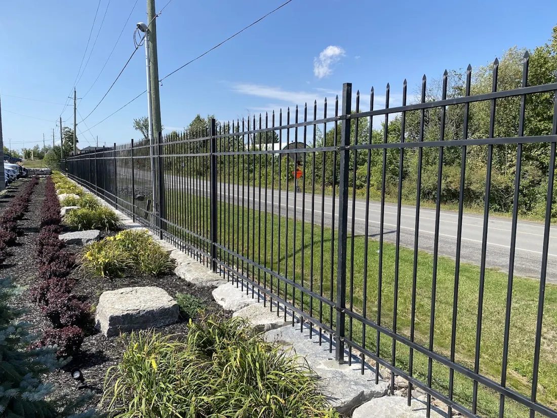 Black aluminum fence running along a landscaped garden bed beside a road