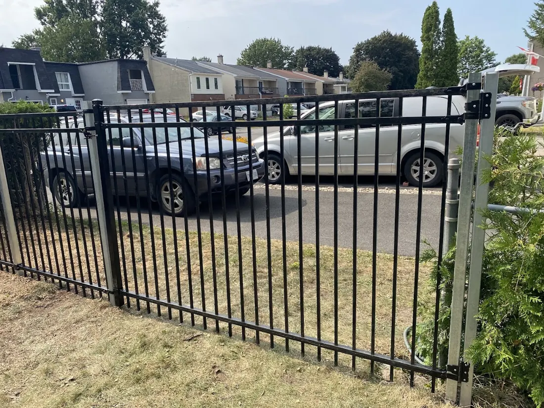 Black wrought-iron style fence along a driveway with parked vans