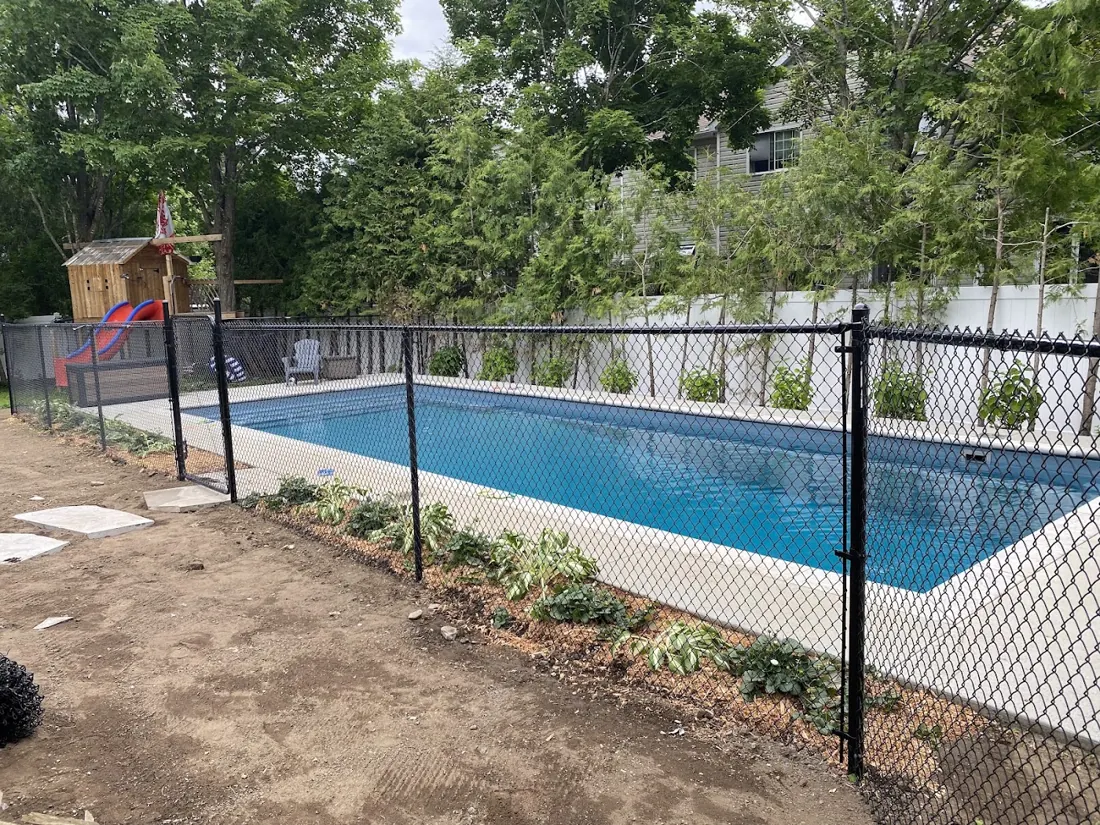 Black pool fence around an in-ground pool with fresh soil in the foreground