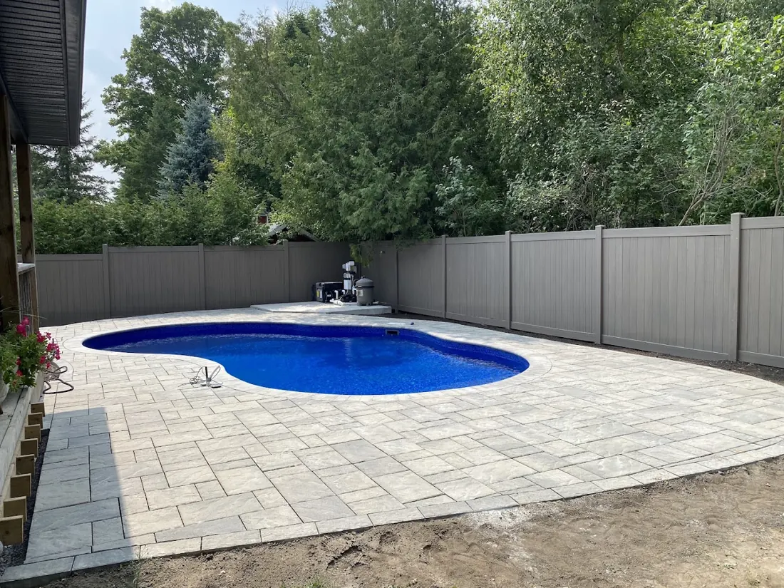 Taupe vinyl fence around a backyard pool with new interlock paving