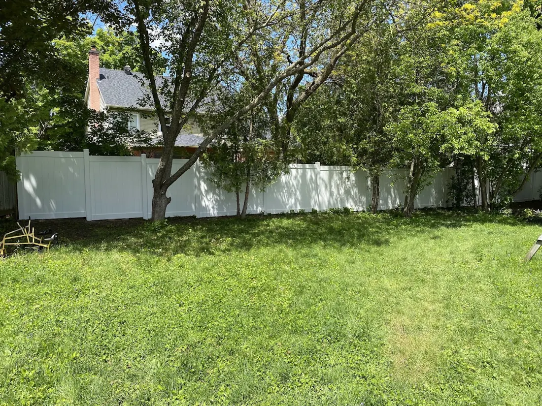 White vinyl fence along the back of a lawn with mature trees